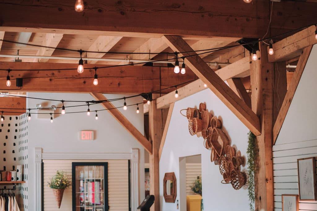 The dining room under exposed timber trusses strung with Edison lights, copper molds on the wall